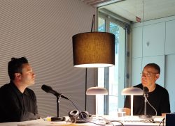 Albert Lladó i Toni Sala conversant davant de micròfons a l'estudi de ràdio de la Biblioteca Gabriel García Márquez amb llums de taula i una làmpada penjant, al costat d’un finestral